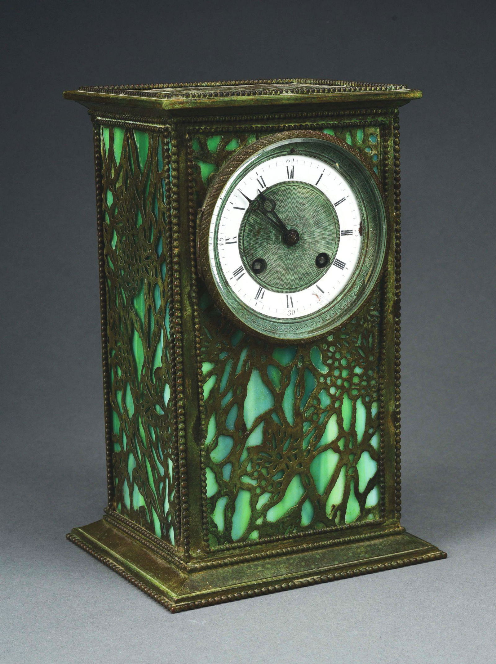 RIVIERE STUDIOS GRAPEVINE CLOCK.: A beautiful slag glass and grapevine overlay clock by Riviere Studios. The 10 - 1/2” tall rectangular clock is comprised of green slag glass, with patinated overlay in a grapevine pattern. The e