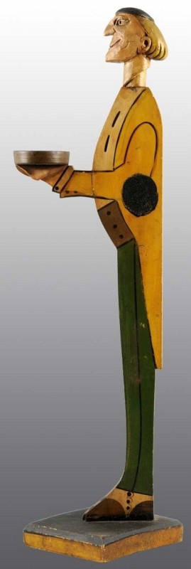 Moxie Man Ashtray Butler in Long Yellow Coat.: Circa 1930s. Moxie advertising is blacked out on either side. Three dimensional carved face and neck. Medium wear, light crazing and soiling. Today, collectors appreciate the folky appeal of these sta