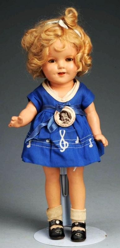 Ideal Composition Shirley Temple.: Circa 1930s. Marked head and body, lashed sleeping eyes, original blonde mohair wig in original set (a little mussed), totally factory original tagged blue music dress, underwear, shoes and socks, ori