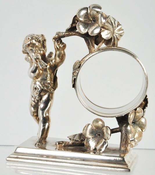 Angel Playing Flute Napkin Ring.: Flowers decorate napkin holder and base. Manufactured by Simpson, Hall, Miller & Co. Size: 4" T.