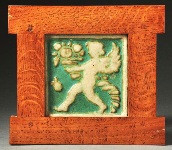 Grueby Faience 2-Color Tile.: Depicts a winged cherub holding a pot of flowers. In a Dard Hunter Studios frame. Size: Framed: 10 - 1/4" x 9 - 3/4".
