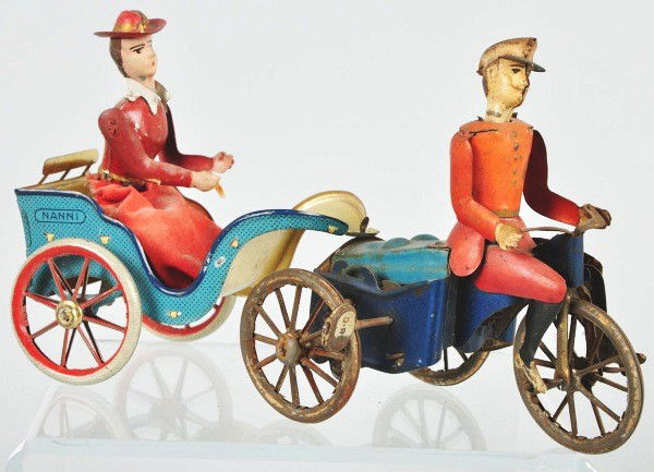 Tin Litho Lehmann Anxious Bride Wind-Up Toy.: German. Working. All original. Lehmann bell mark on rear. Two piece toy with man pulling bride in cart. Some wear to figure on front and woman missing cloth tissue. Size: