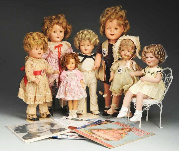 Lot of 7: Shirley Temple Dolls.: New bisque Shirley sitting in a chair; 1958 vinyl Ideal Shirley (some hair plugs missing); 4 Ideal composition 1930s Shirleys, 1 with replaced wig, all with crazing and wear; 1 Shirley unmarked Look A