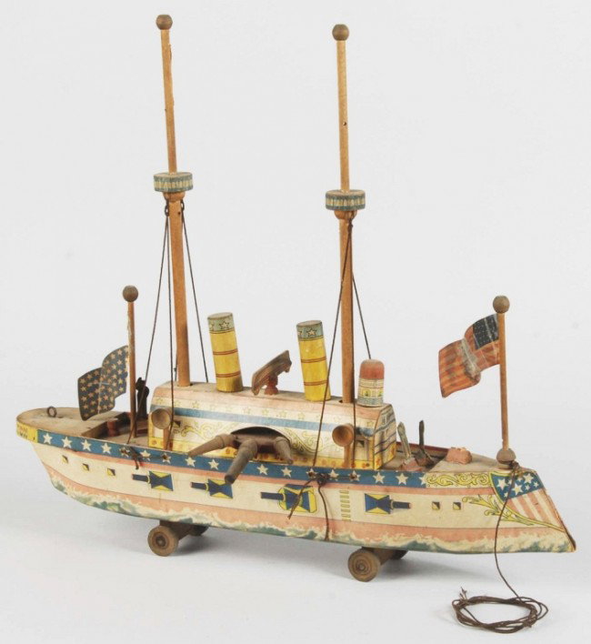 Early Paper on Wood Battleship Toy.: American. Probably Reed or Bliss. Marked "The US Cruiser Boston". Original masts and wooden cannons. One flag is detached but present and some fading to paper. Size: 19" L. Condition: (Very Good).