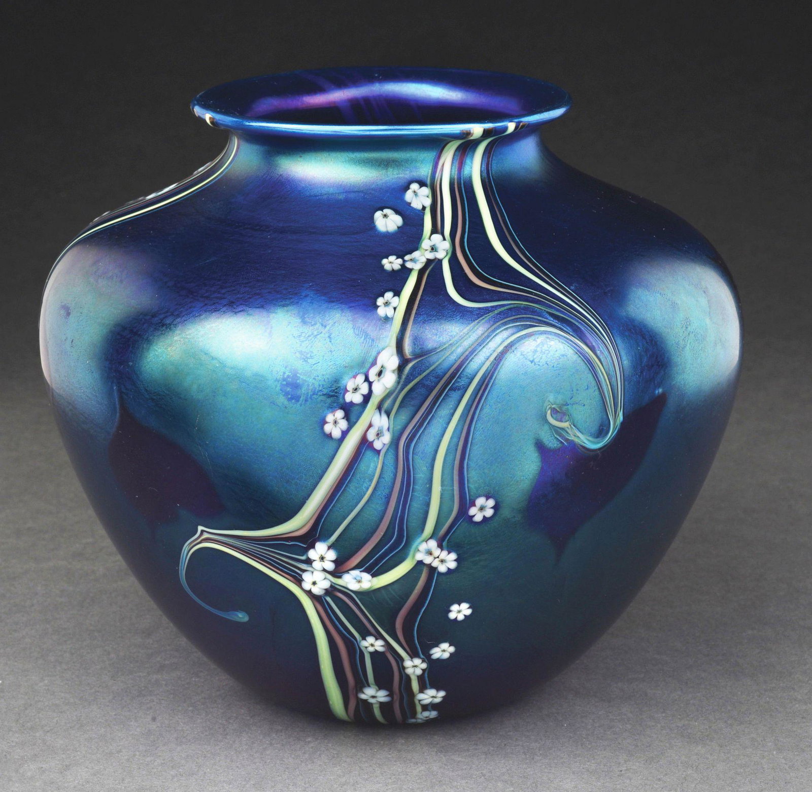 ORIENT AND FLUME IRIDESCENT VASE.: A beautiful iridescent vase by Orient and Flume. The vase stands 6" and features a background of intensely iridescent purple glass. It is decorated with small white flowers and abstract swirling lines