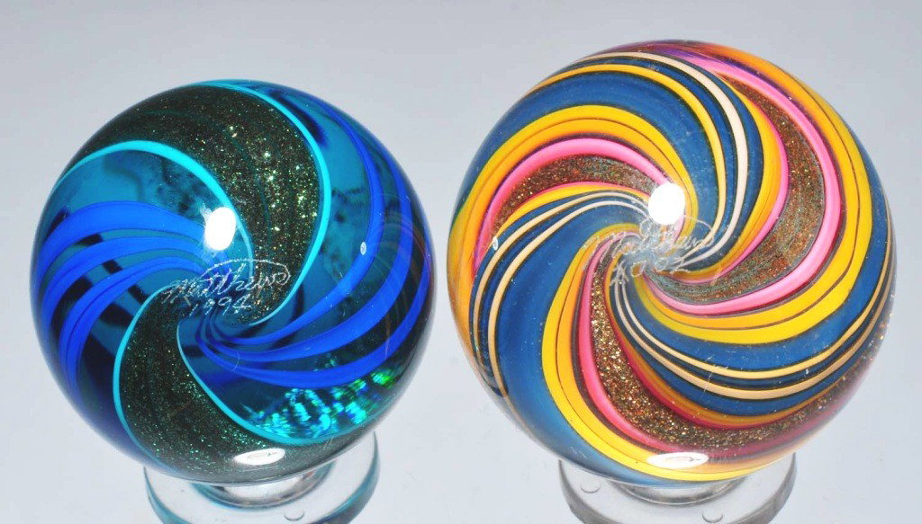Lot of 2: Mark Matthews Contemporary Marbles.: Includes one signed Matthews 1994 with blue striped lutz pattern and one sighed Matthews 2002 in multi-striped lutz with blue, yellow, and pink pattern. 1 - 1/8" and 1 - 1/4" Dia. Condition: (9.5).