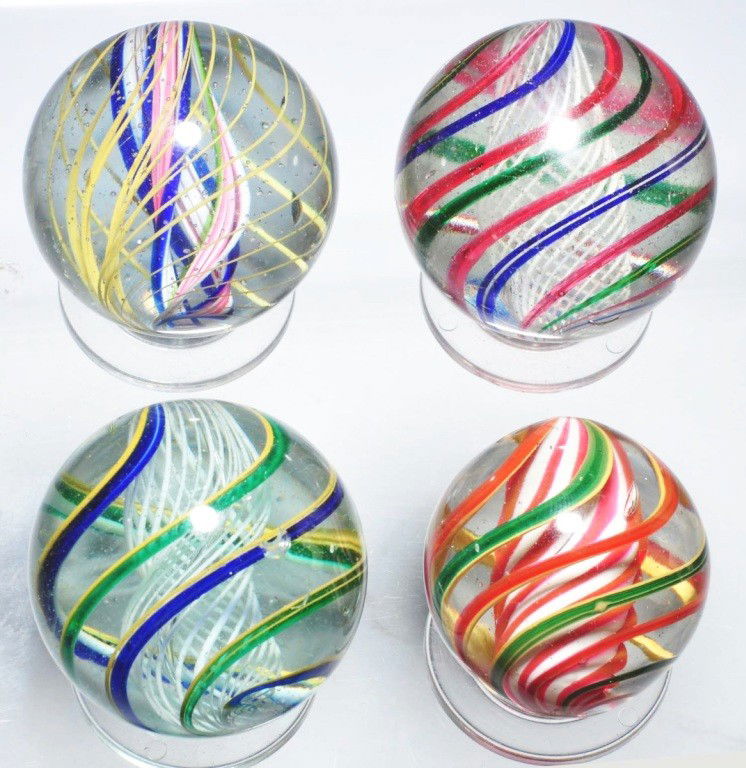 Lot of 4: Large Swirl Marbles.: Largest is a white latticino with outer alternating bands of blue/yellow and translucent green/yellow. Smallest is a beautiful white solid core overlaid with red bands and outer bands of alternating r