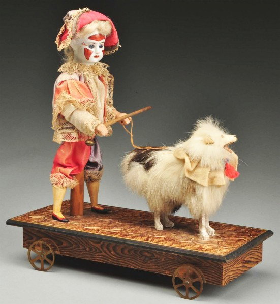 Mechanical German Pull Toy.: Bisque head boy in painted clown face wearing original clown costume. When toy is pulled boy moves his head and prods dog with stick. Papier-mâché dog is fur-covered. Needs slight adjustment of unde