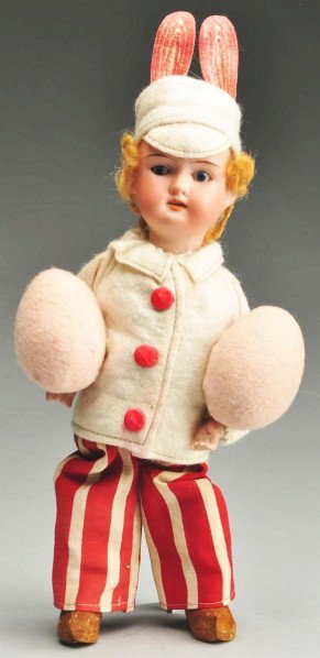 Mechanical Easter Bunny Toy.: Bisque socket head marked 7/0 with glass eyes, open mouth, and blonde mohair wig. Mechanical cardboard body toddles from side to side, wire arms, wood legs and composition shoes. Original clothing and