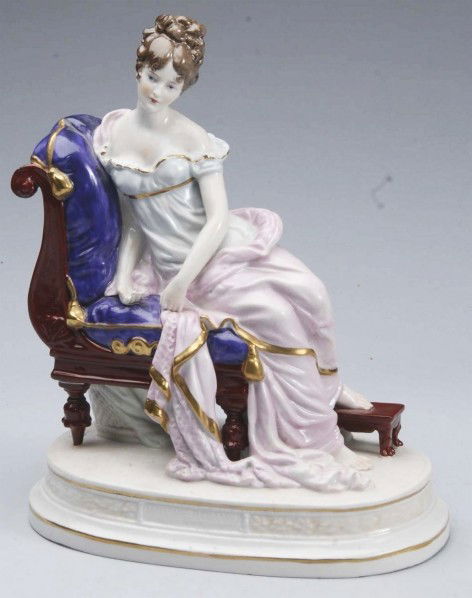Sitzendorf Porcelain Figurine.: German china lady sitting on a couch, lovely face and hairstyle with curls on her head and tendrils around her face, flowing pink and blue robe. Marked with blue S in crossed swords, Sitzendorf logo.
