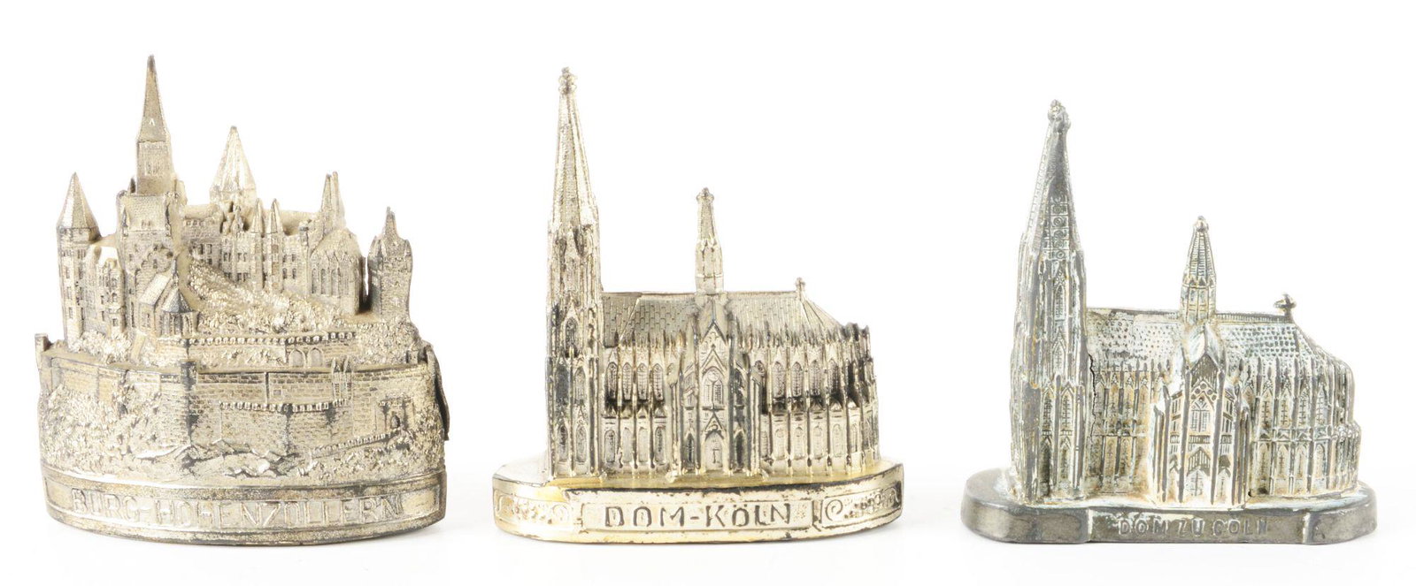 LOT OF 3: GERMAN WHITE METAL CASTLE BANKS.: All three have original traps. One is marked "DOM - KOLN". One marked "BURG - HOHENZOLLERN." has a mold flaw and small piece missing. The last one is marked "DOM- ZUCOLN." Condition: (Very Good). Dime