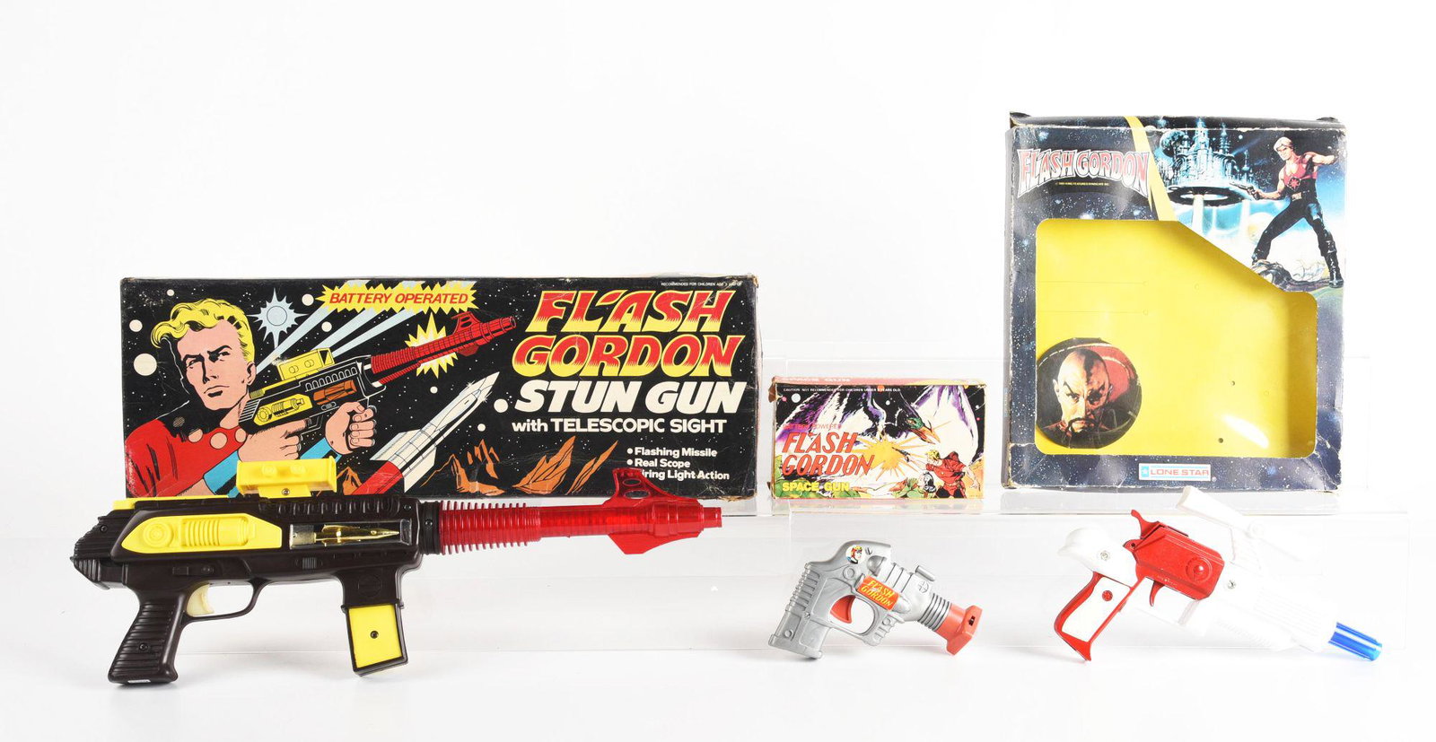 LOT OF 3: DIE-CAST & PLASTIC AMERICAN & ENGLISH-MADE FLASH GORDON GUNS.: All in original boxes. One is an English-made Lone Star, the other two are a battery-powered American-made Space Gun pistol and a battery-operated Stun Gun with telescopic sight. Boxes have some creas