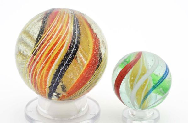 Lot of 2: Swirl Marbles.: Description The smaller marble is a three stage marble with a solid yellow core surrounded by white latticino. Outer decoration is orange, white, green, and blue bands. The larger marble is a multicol