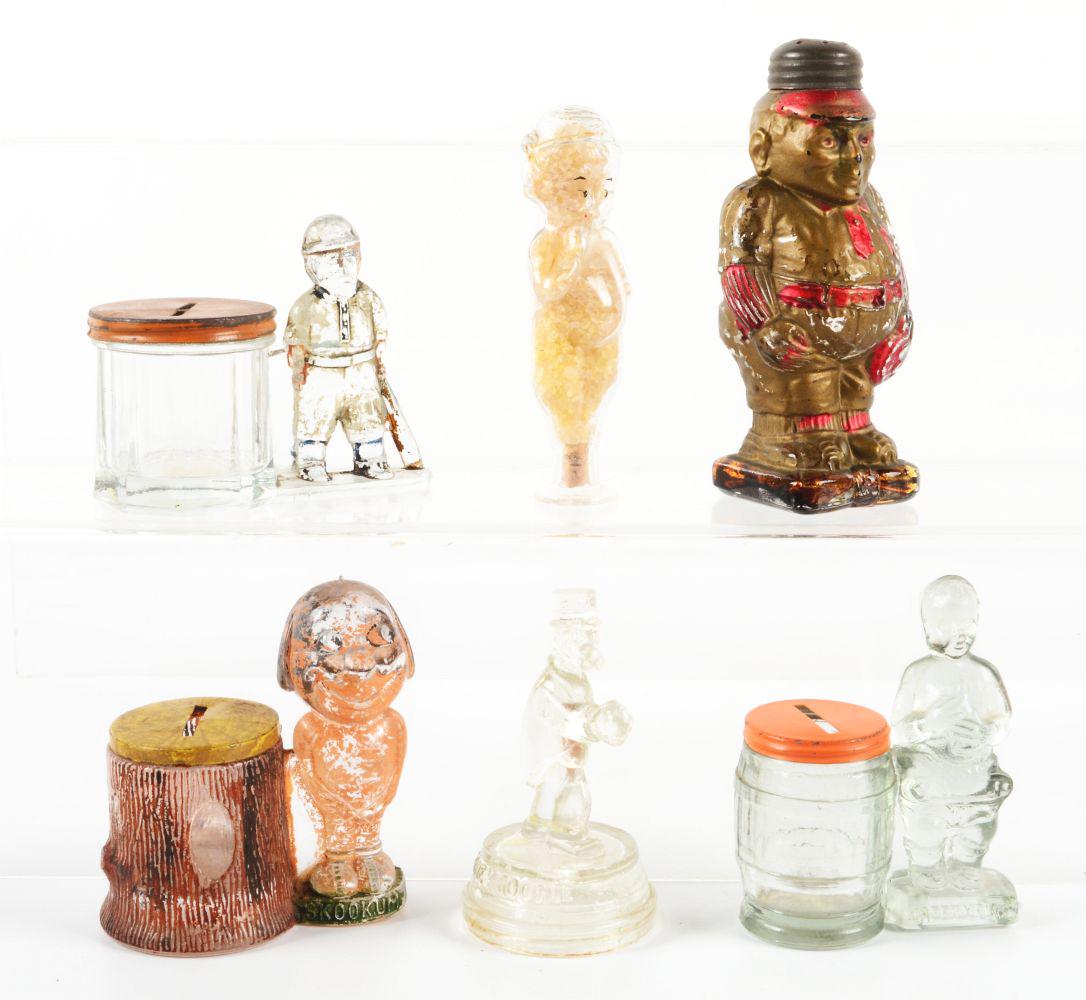LOT OF 6: VINTAGE GLASS CHARACTER CANDY CONTAINERS.: Lot of six candy containers consists of: (A) Skookum by tree with metal closure; (B) child with container next to him with metal closure; (C) a rare boy with baseball bat and container beside him, wit