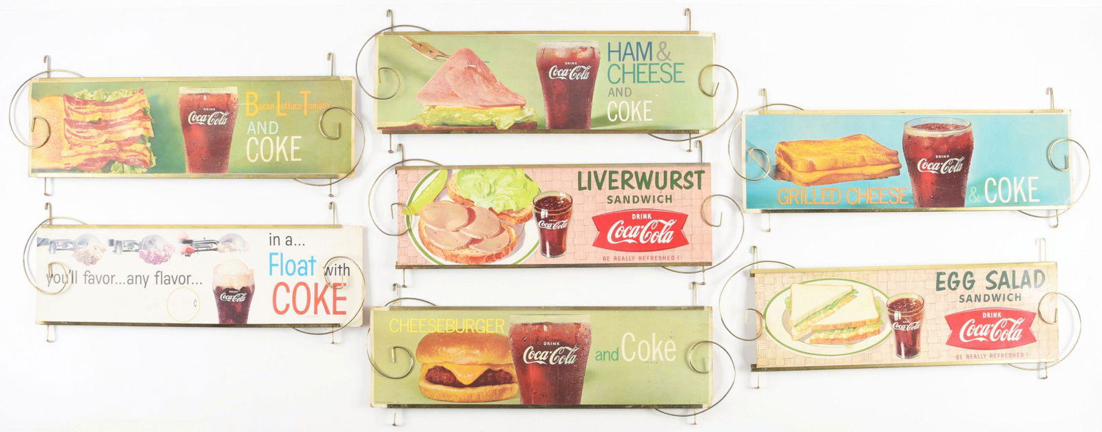 COLLECTION OF 7 COCA-COLA CARDBOARD LITHOGRAPH CHANNEL SIGNS W/ ORIGINAL METAL DISPLAYS. (1 of 2)