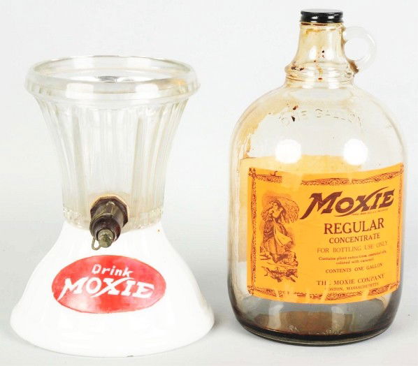 Moxie Gravity Syrup Dispenser.: 1940s. Milk glass and glass with moderate wear and soiling. Also includes a paper-labeled one-gallon jug that would display inverted in the dispenser. Moderate overall wear with syrup residue remainin