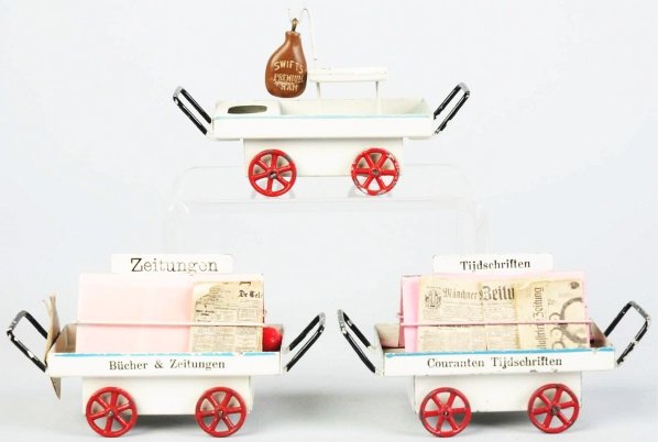 Lot of 3: Marklin News & Fruit Carts.: German. Circa 1930s. Includes one fruit cart with a piece of ham but missing some fruit. Both newspaper carts are marked "Marklin Made in Germany" on bottoms. Some paint chipping and wear throughout. 