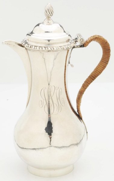 A Silver Hot Water Jug.: With marks for Whipham & Wright, London 1760, the baluster body with a short spout, the lower front engraved with crest and the side with later initials, a caned handle, and on a short plain foot, the