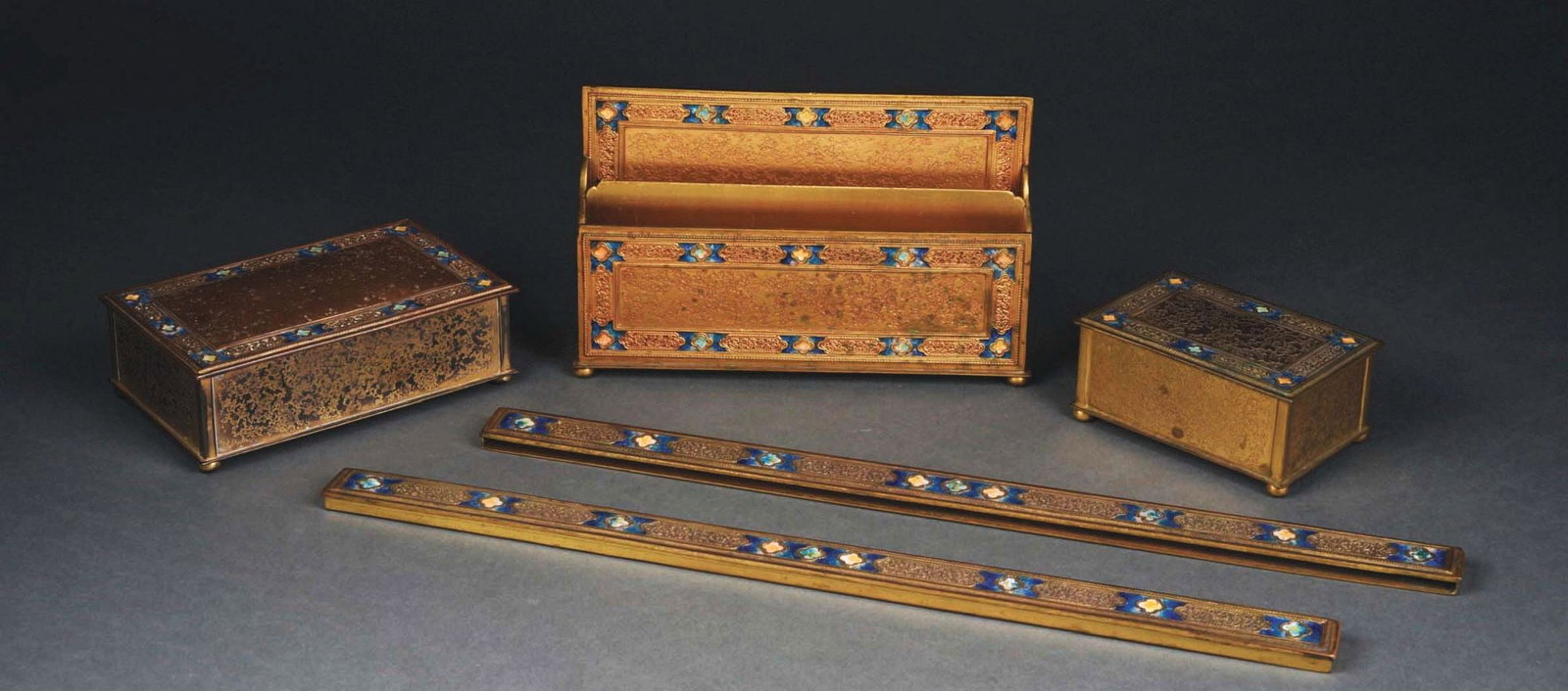 TIFFANY STUDIOS ENAMEL 5-PIECE DESK SET.: A gorgeous five-piece desk set by Tiffany Studios in gold doré with blue enamel. The set includes stamp box (384), letter holder (386), pair of blotter ends (383) and enameled cigarette box with 