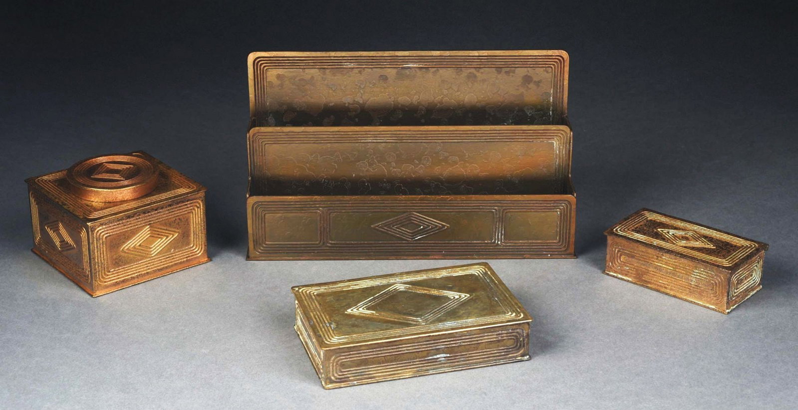 TIFFANY STUDIOS 4-PIECE "GRADUATE" DESK SET: A lovely four-piece desk set by Tiffany Studios. Each of the four pieces has the "Graduate" pattern. The pieces are finished in acid-etched gold. The set includes stamp box (1797), medium lidded box (
