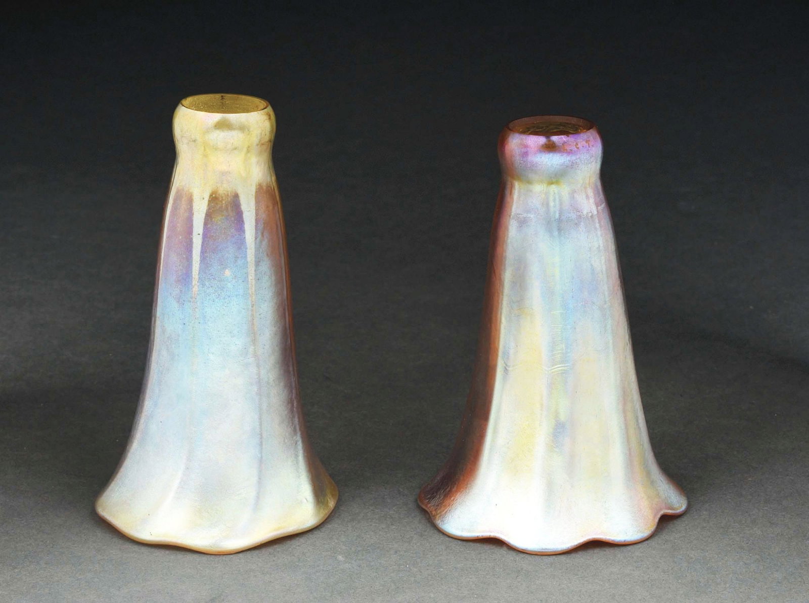 LOT OF 2: TIFFANY STUDIOS GOLD LILY SHADES.: A beautiful pair of lily shades by Tiffany Studios. Both shades are composed of Favrile glass in gold with iridescent tones of purple, pink and blue. Both shades are ribbed, having slightly ruffled mo