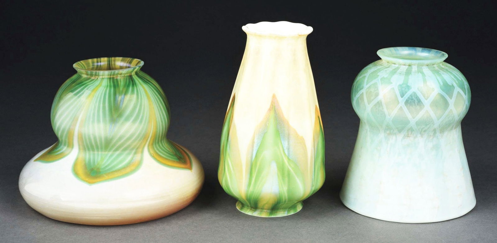 LOT OF 3: TIFFANY STUDIOS FAVRILE GLASS SHADES.: A lovely set of three Favrile shade by Tiffany Studios. (A) Bell-shaped shade with a cream-colored background and green pulled feather motif. The shade is signed "L. C. T." and is in excellent conditi