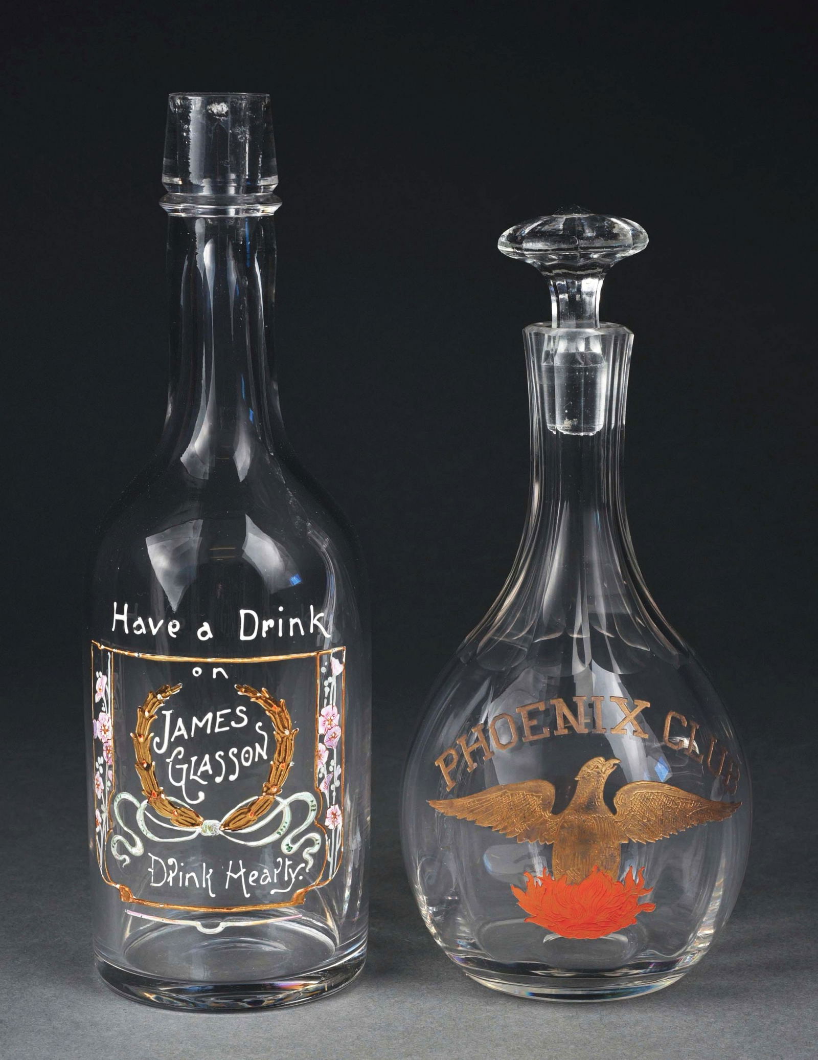 LOT OF 2: PRE-PROHIBITION BOTTLES: (A) "James Glasson" embossed on hand-blown clear glass with gold and white. 11"h. No damage. (B) "Phoenix Club" decanter with embossed painted eagle. Hand-blown with pontil. 10"h. No damage. Condition
