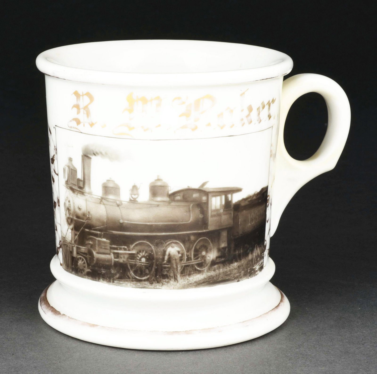 PHOTOGRAPHIC TRAIN IMAGE SHAVING MUG.: Has the name "R.M. Baker" in gold gilt. Mug is signed "George E. Wagner & Company Saint Joe" under base. Beautiful photographic image of man standing in front of steam engine. Condition: (Excellent). 