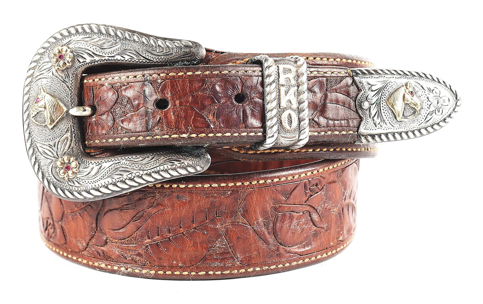 ROSE ORTEGA'S PERSONAL VISALIA RANGER BELT AND BUCKLE: Well maker-marked floral carved ranger-style Visalia belt with sterling three-piece buckle with rose gold horseheads inset with rubies. Rose’s initials "RKO" are raised in gold letters on the ke
