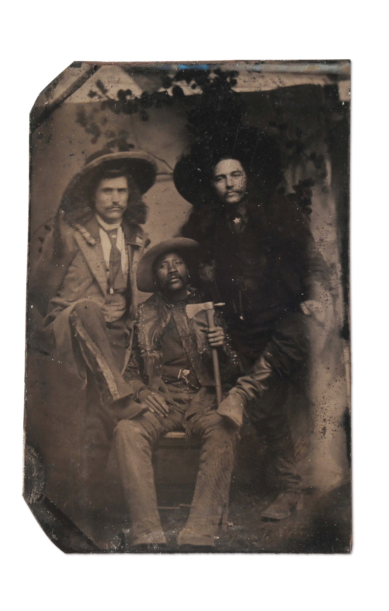 A TINTYPE OF THREE WESTERN SCOUTS OR FRONTIERSMEN: A 3 1/4" x 2 1/8" ferrotype of three men dressed in frontier garb. It is a wonderful image of two long-haired frontiersmen standing with their boots on the knee of a seated black man dressed in fringe
