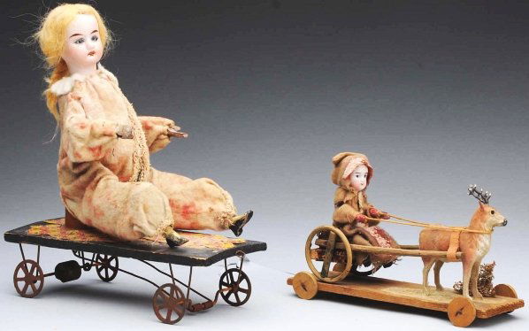 Lot of 2: German Pull Toys.: Wooden platform toy with tin wheels, clown doll with bisque head and original outfit, one arm and legs and head move (rust, soil). Girl with bisque head riding in a carriage pulled by a reindeer, all