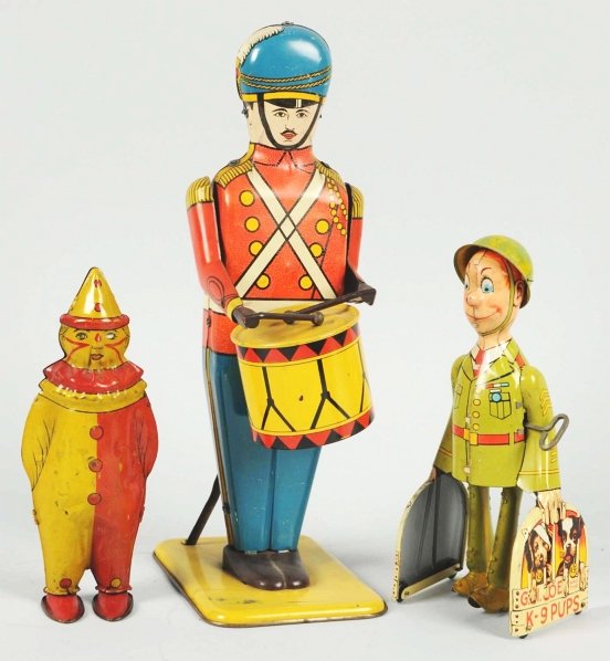 Lot of 3: Tin Litho Figural Wind-Up Toys.: American. Working. Includes one No. 27 Drum Major by Wolverine, one Unique Art GI Joe and the K-9 Pups, and one Lindstrom Johnny the Clown. Some overall scratching and wear. Condition (Very Good - Exc