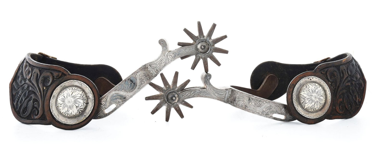 OVERLAID CALIFORNIA SPURS: Fully engraved overlays in a scroll pattern. Floral carved two-piece leathers with domed Bohlin-style engraved 1 5/8" silver conchos. Fine condition. Circa 1950s, tie down slots cut into the bands. Pr