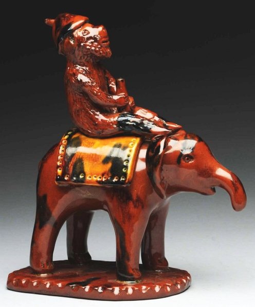 Unusual Lester Breininger Figural.: Depicts a monkey riding an elephant on an incised base. Repair to feather in the monkey's cap. Condition (Excellent). Size 9" T.