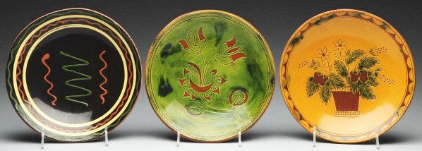 Lot of 3: Lester Breininger Redware Plates.: Includes one with original slipware decoration in greens, oranges, and yellows, one with a folky tulip, and one with a pot of flowers. Condition (Excellent). Size Each: 10 - 1/2" Dia.