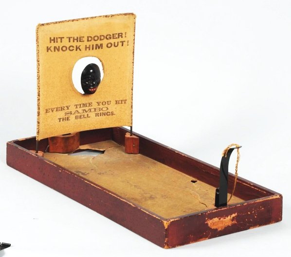 Early African American Bell Ringer Game.: Wood and pressed cardboard game. Balls are hit at tin Sambo figure that pushes back to ring bell. Marked "Hit the Dodger! Knock Him Out!". Small section of flooring is missing. Condition (Very Good - 