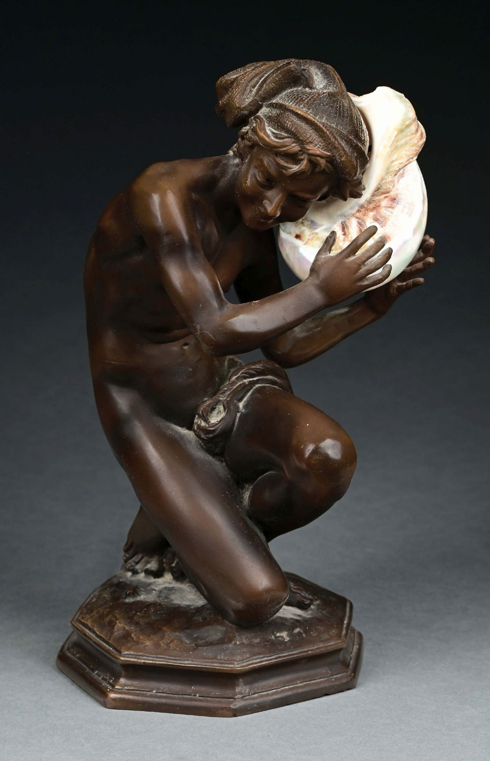 AFTER GUSTAV GURSCHNER FIGURAL BRONZE TABLE LAMP: A beautiful figural bronze table lamp after Gustav Gurschner. The 15" tall patinated bronze features a nude male figure holding a large iridescent shell to his ear. The shell has an internal light bul