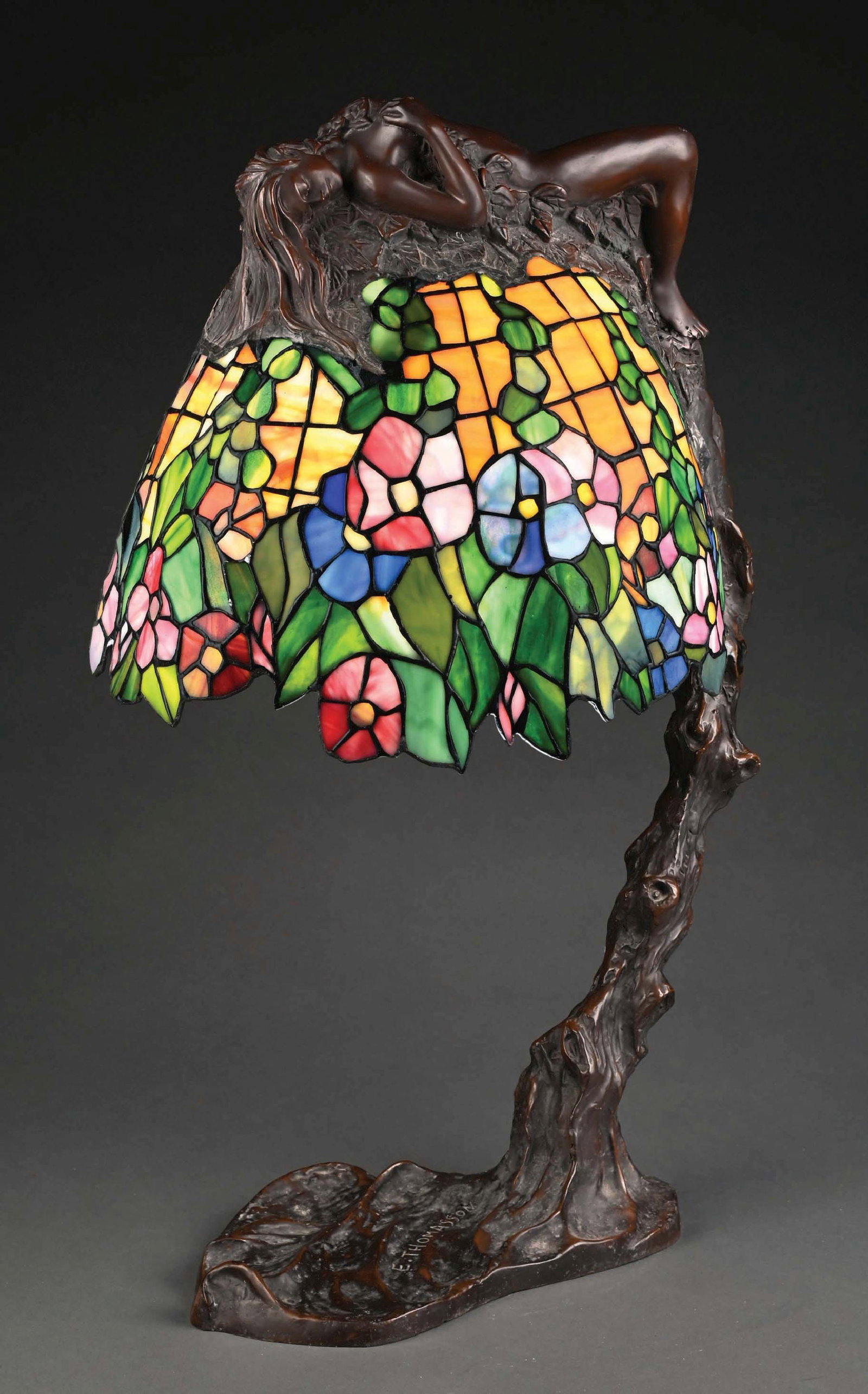 AFTER E. THOMASSON "DAPHNE" TABLE LAMP: A beautiful example of the iconic “Daphne” table lamp after E. Thomasson. The floral shade with caramel background and multicolored flowers throughout. With patinated bronze nude draped ov