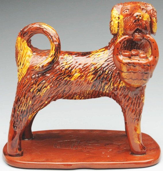 Wonderful Lester Breininger Redware Figural.: 7 - 1/4" T. Depicts a standing dog holding a basket of apples in his mouth. Attached to an incised decorated base. (Near Mint Plus).