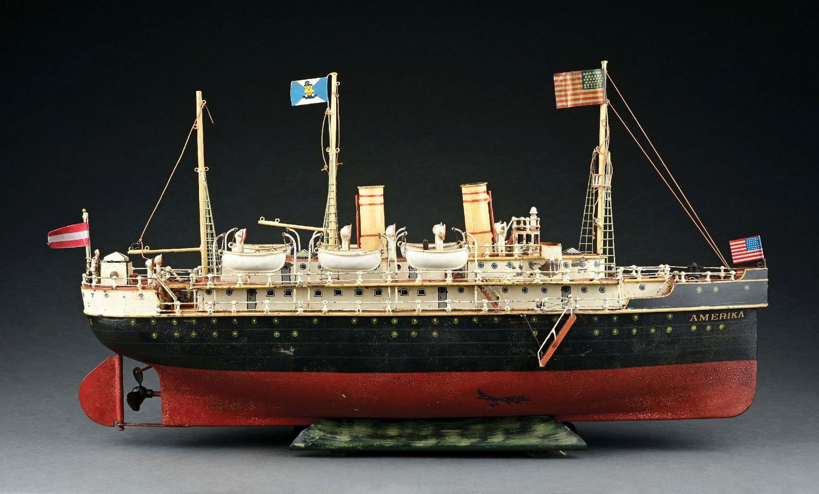 MARKLIN CAT. REF. 5050 "AMERIKA" 1ST SERIES W/ CLOCKWORK POWER: C. 1909. CONDITION: Boat retains original stand, mast and life boats. Some paint crazing to red section of hull and a few blemishes; the rest of the boat is in excellent condition. Two replacement fla