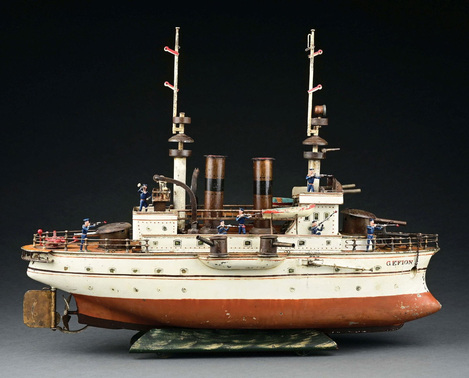 MARKLIN CAT. REF. 1091 "GEFION" BATTLESHIP W/ CLOCKWORK POWER: C. 1904. CONDITION: Mast flags replaced. Missing chains for cranes. Lacking one lifeboat. Does retain an original lifeboat and stand. This boat is included with 11 original Heyde original sailors. Ori