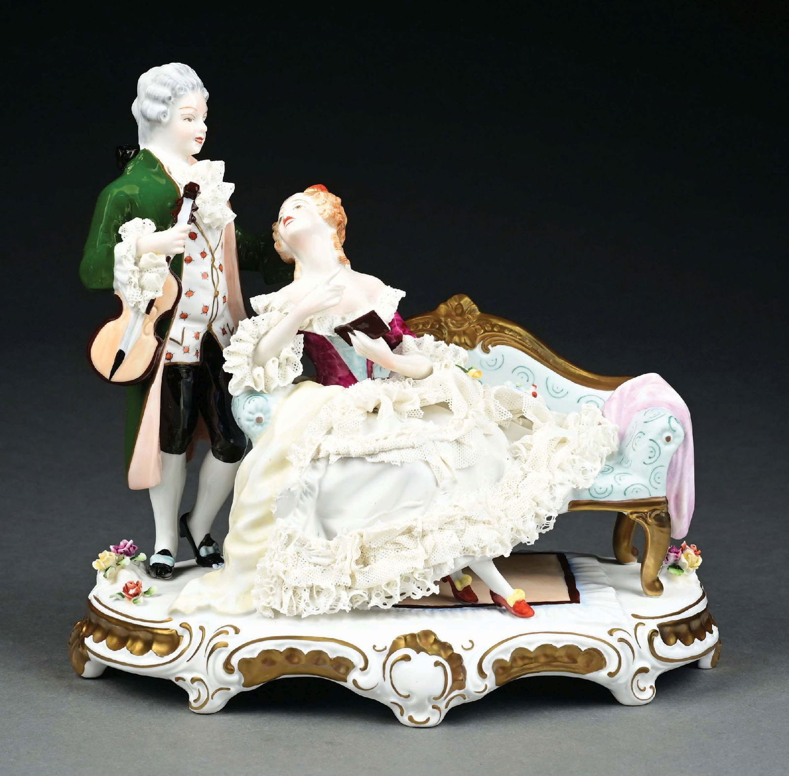DRESDEN STANDING GENTLEMAN & LADY SEATED ON LOVESEAT FIGURINE: Has Dresden stamp under base. Damage to lace. Condition: (Good). Dimensions: 10" x 5" x 9 - 3/4".