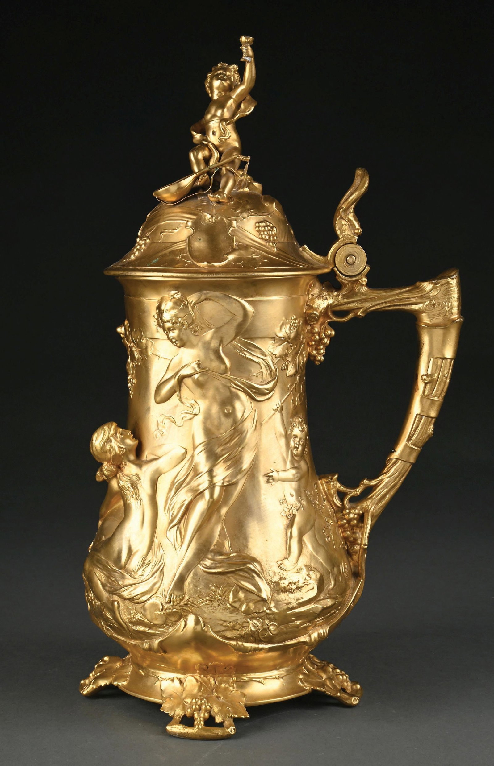 WMF BRASS GOLD WASHED STEIN: Art Nouveau-style German WMF stein or tankard with reliefs depicting cherubs, fruits, nymphs, and maidens. Cherub figure topper. Condition: (Excellent). Dimensions: 7" x 7" x 16".