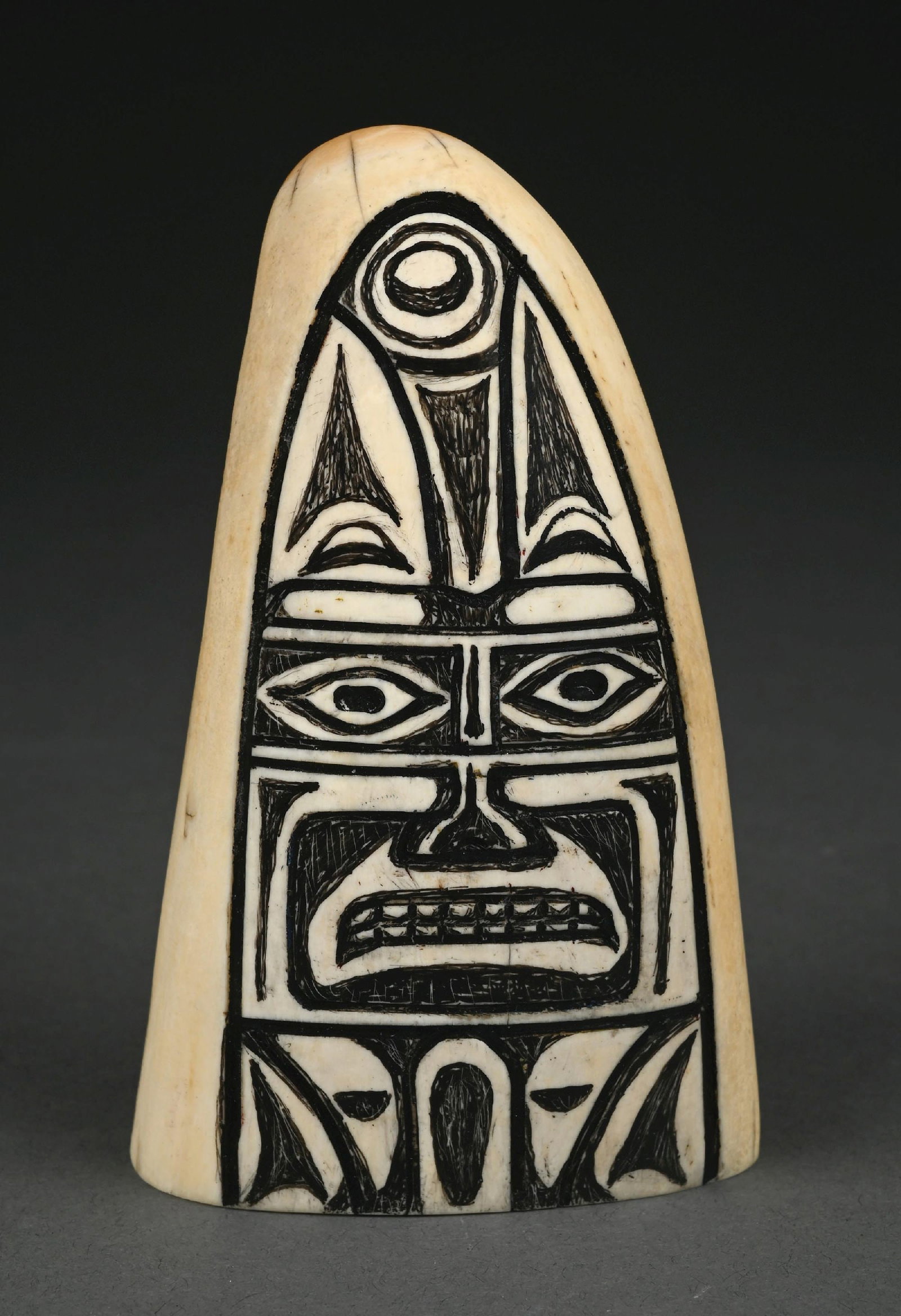 NORTHWEST COAST NATIVE CARVED TOTEM WHALE TOOTH: 20th century northwest coast carved whale tooth with totemic design. Measures 4-1/2" x 2-3/4". Condition: (Very Good-Excellent). Dimensions: 4 -