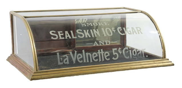 COUNTERTOP CURVED GLASS SHOWCASE ADVERTISING SEALSKIN CIGARS: C. 1910. CONDITION: It shows all original German silver covering with original glass and backdoors. It shows a small 3" crack to the corner glass on the curved glass to the lower left-hand corner. It