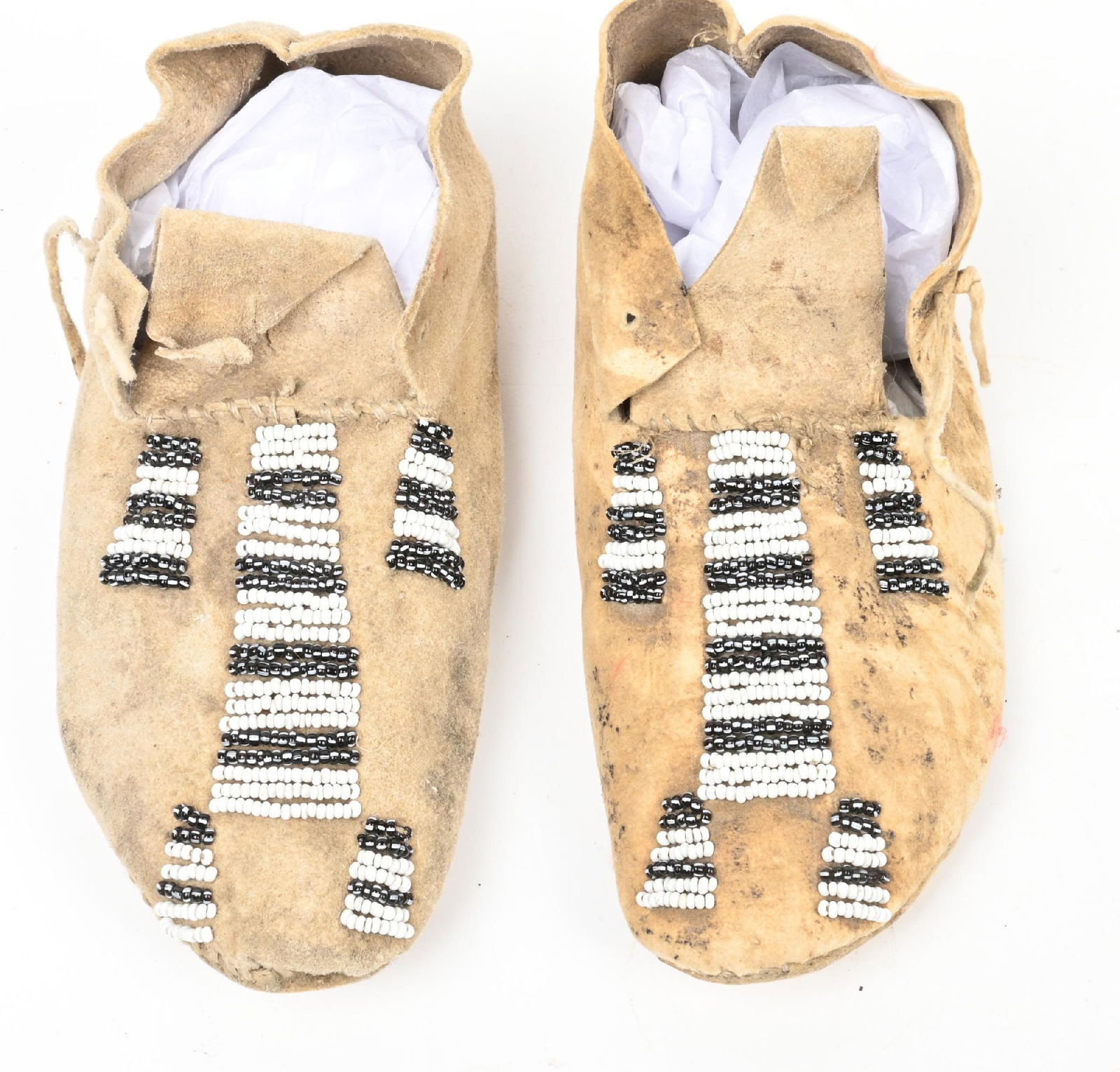 BLACK AND WHITE BEADED BABY MOCCASINS: Rawhide soles. 5 3/4" length. CONDITION: Good. Dimensions: 5 3/4" L.