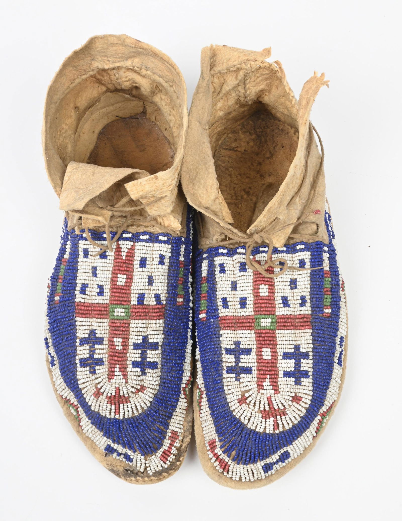 ARAPAHO BEADED MOCCASINS: Sinew sewn on Indian tanned buckskin with cross patterns of white heart rose, grass green, and white. 9 1/4" length. CONDITION: Very good with a small tear in the buckskin on the upper top of the left