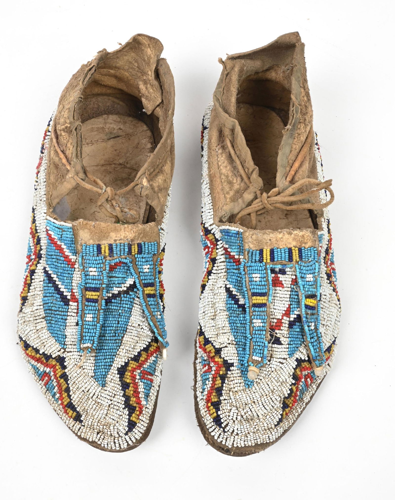 LIGHT BLUE & WHITE BEADED MOCCASINS: Northern Plains beaded men's moccasins. Geometric designs with bifurcated tongues on Indian tanned buckskin. Rawhide soles. CONDITION: Very good. Dimensions: 11" L