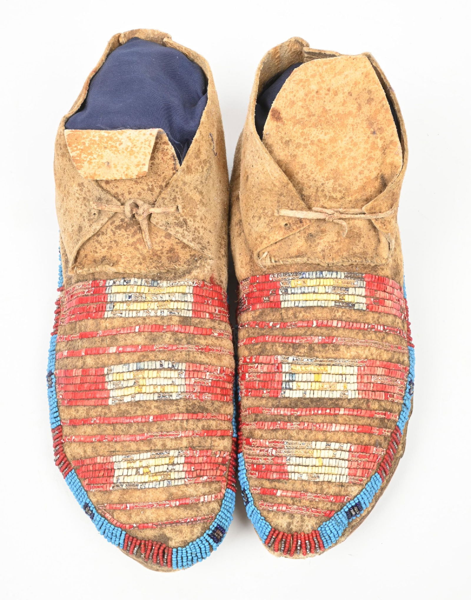 BLUE & RED STRIPED LIGHTLY BEADED MOCASSINS: Lakota moccasins with quilled bands. Beaded designs of light blue, red, dark blue, and silver faceted beads on Indian tanned buckskin with rawhide soles. CONDITION: Good. Some light bug damage to quil
