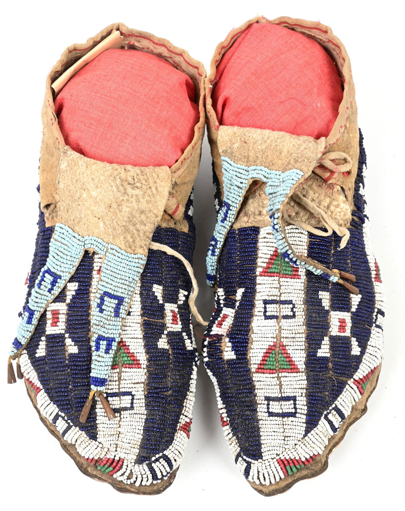 BLUE AND WHITE GEOMETRIC PATTERN MOCCASINS: Circa 1880s Lakota moccasins on Indian tanned buckskin with rawhide soles. Sinew sewn beaded geometric patterns of dusty green, white heart rose, and translucent dark blue on white fields. Bifurcated